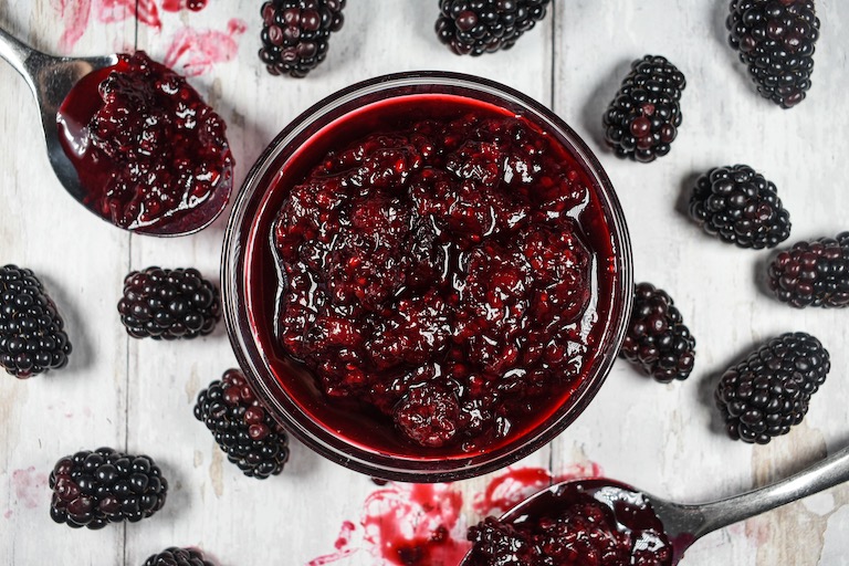 A small dish of blackberry compote surrounded by fresh blackberries