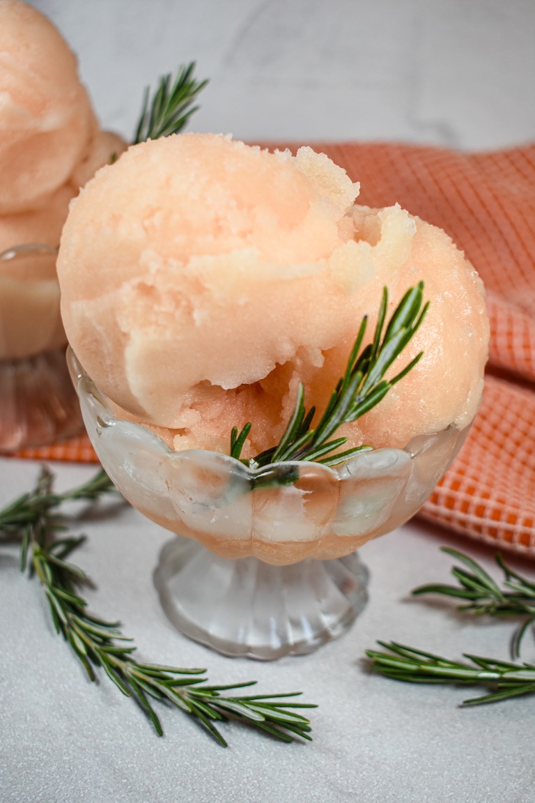 A glass dish of grapefruit sorbet garnished with rosemary