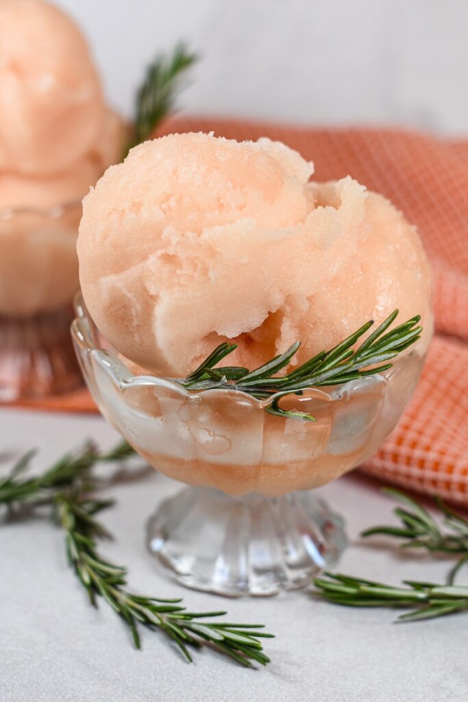 A dish of grapefruit sorbet garnished with sprigs of fresh rosemary