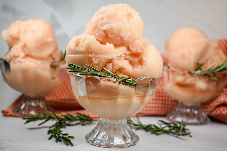 Glass dishes of grapefruit and rosemary sorbet on a white surface