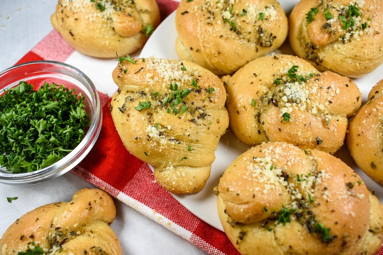 A plate of homemade garlic knots with a dish of chopped parsley