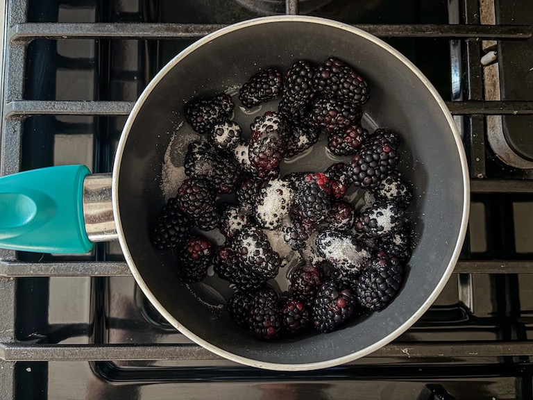Blackberries and sugar in a small pan on the stovetop