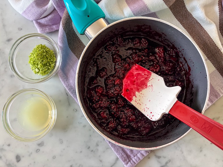 A pan of blueberry compote, dishes of lime zest and juice, and a spatula