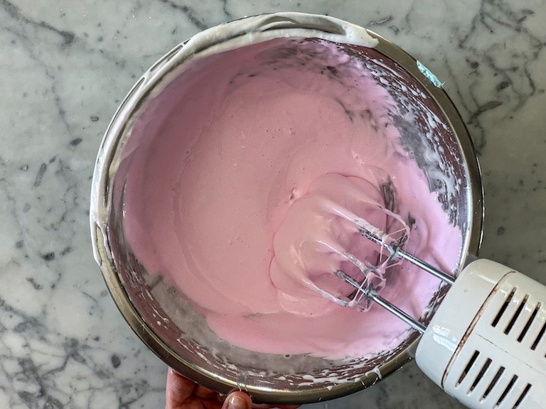 Mixer mixing pink marshmallow fluff in a metal bowl