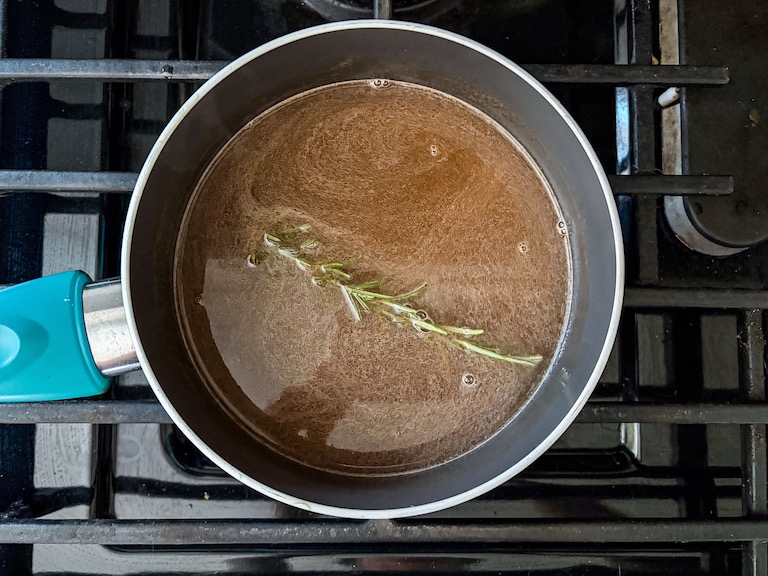 Infusing a sprig of rosemary into a pan of grapefruit juice