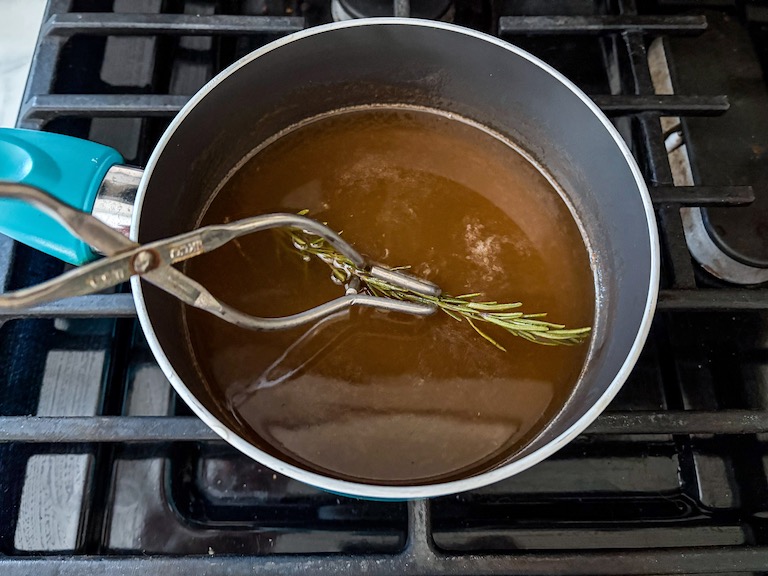 Tongs removing rosemary from a pan of grapefruit juice