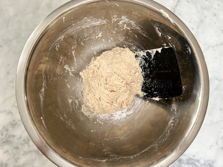 Dough ingredients in a bowl with a bench scraper