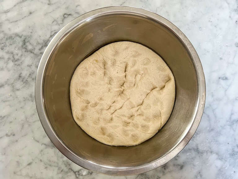 punched-down pizza dough in a metal bowl