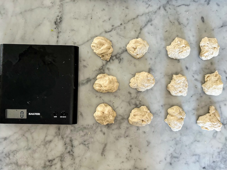 Balls of dough arranged on a marble surface next to a kitchen scale