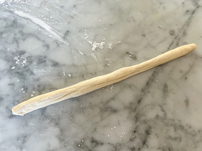 A tube of pizza dough on a marble surface