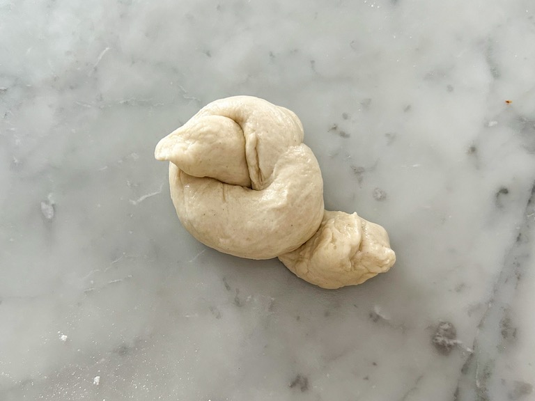 An unbaked garlic knot on a marble surface
