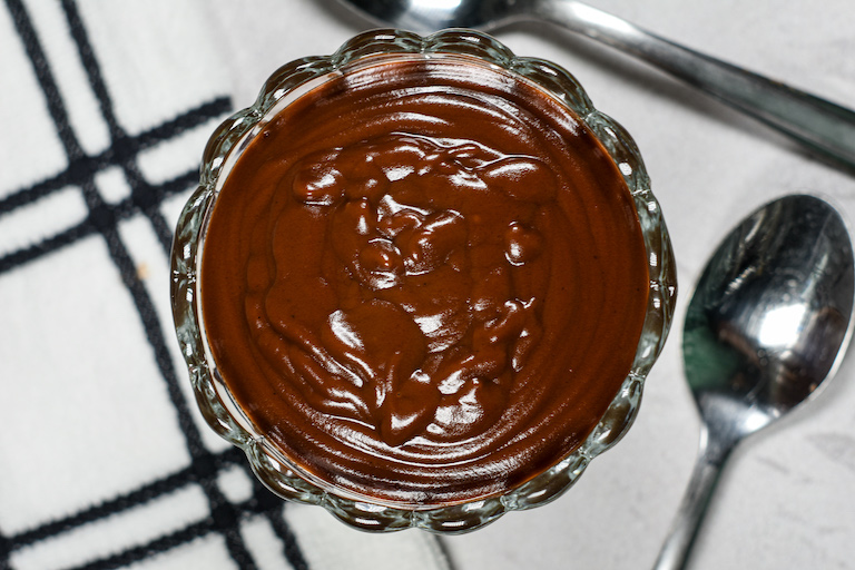 A dish of hot fudge sauce on a plaid towel with a spoon