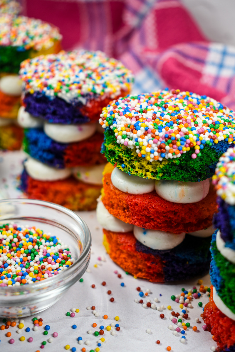 Rainbow dot cakes arranged on a white surface with a dish of rainbow nonpareils