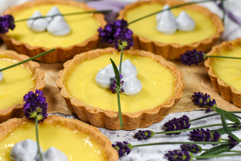 Horizontal shot of miniature lavender lemon tarts on a white surface with fresh purple lavender flowers