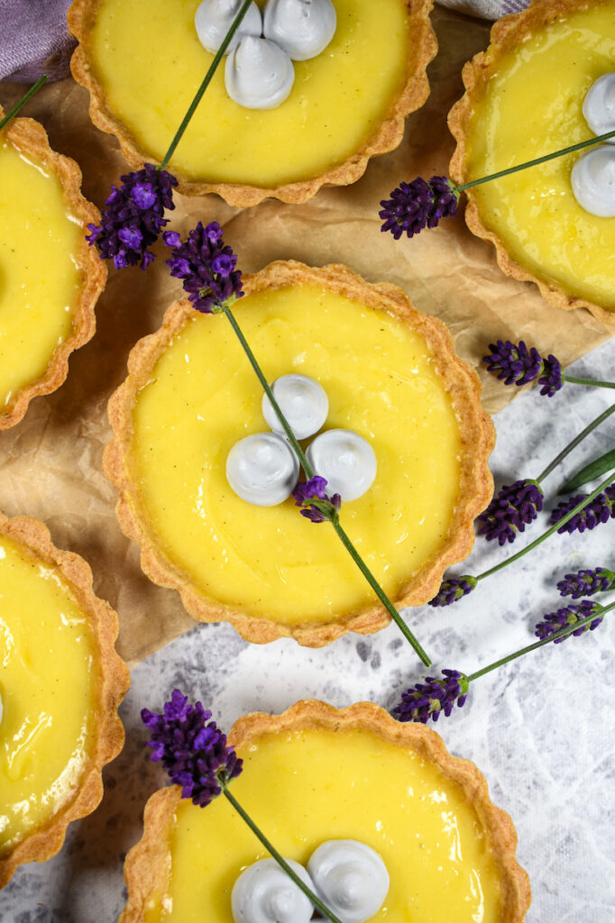 looking down at mini lemon tarts arranged on a white surface with fresh purple lavender flowers