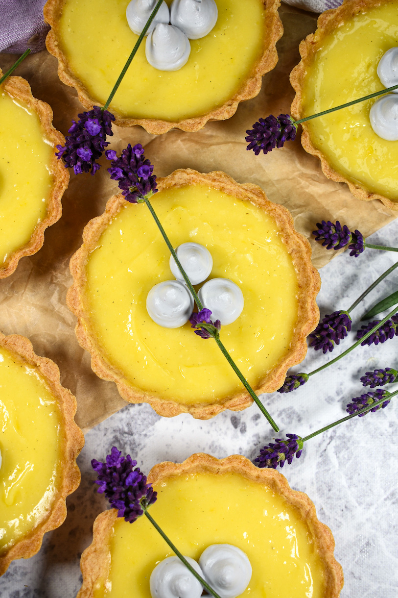 Lavender lemon tartlets arranged on a white surface with sprigs of fresh lavender