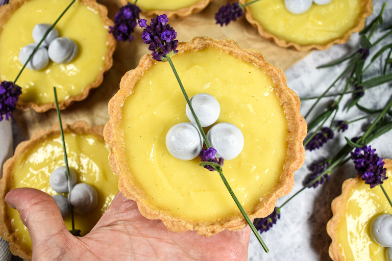Hand holding a mini lemon tart decorated with lavender flowers and lavender whipped cream