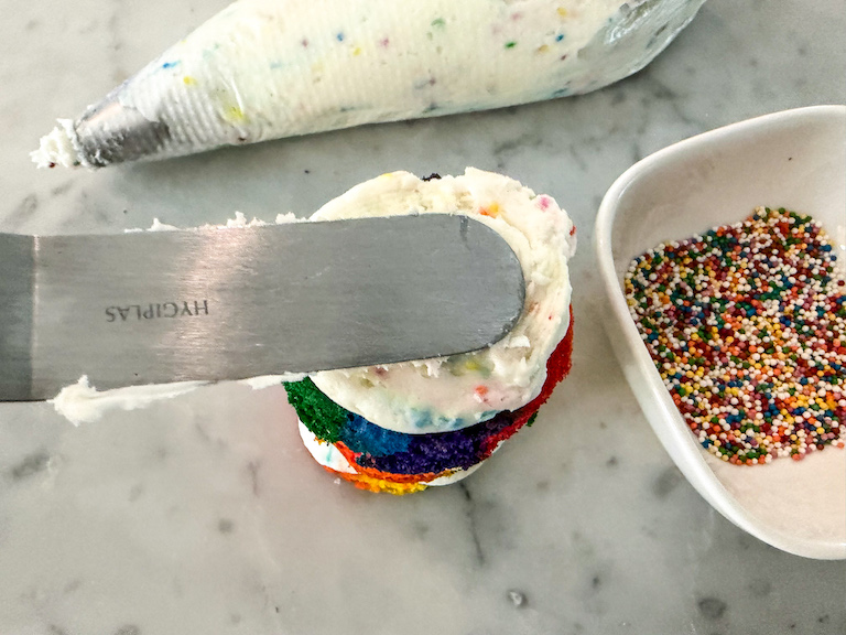 Palette knife spreading buttercream on a miniature rainbow layer cake