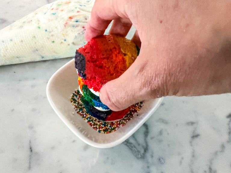 Hand dunking a dot cake in sprinkles
