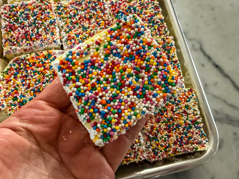 Hand holding a birthday cake marshmallow coated in rainbow sprinkles