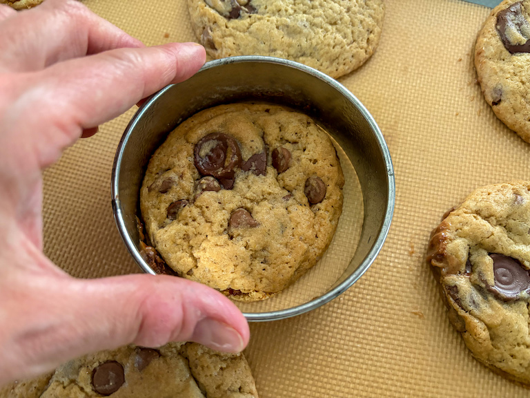 Hand reshaping a cookie with a metal cutter