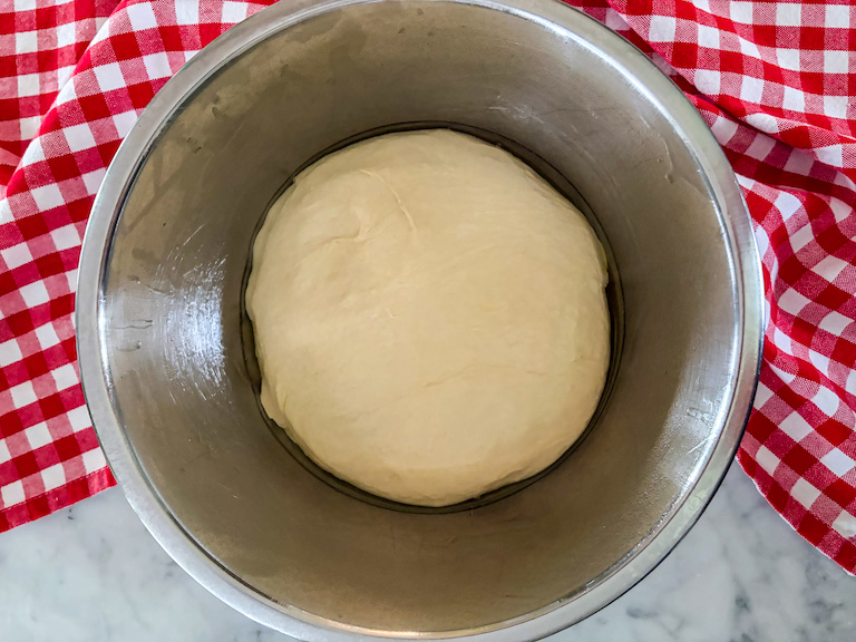 Homemade pizza dough rising in a metal bowl