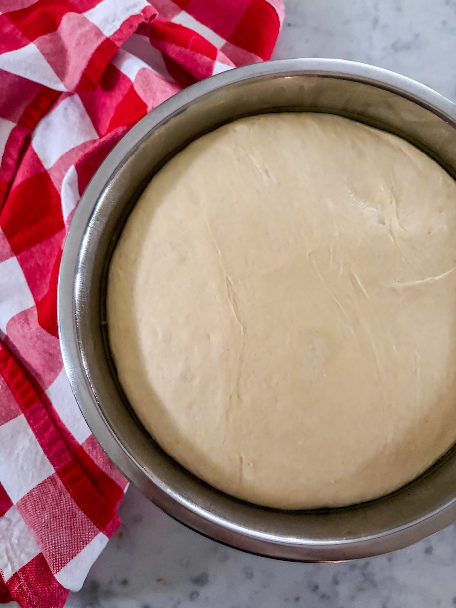 A bowl of pizza dough with a red checkered towel