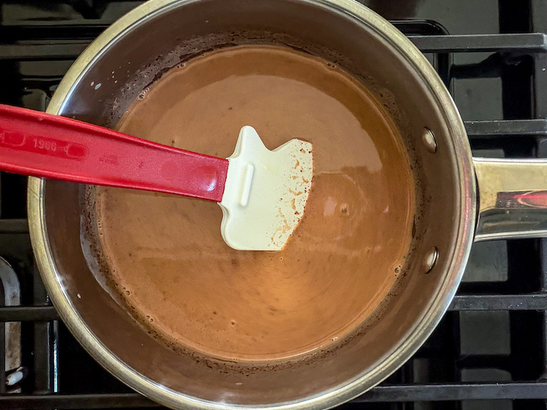 Spatula stirring evaporated milk and chocolate in a pan on the stovetop