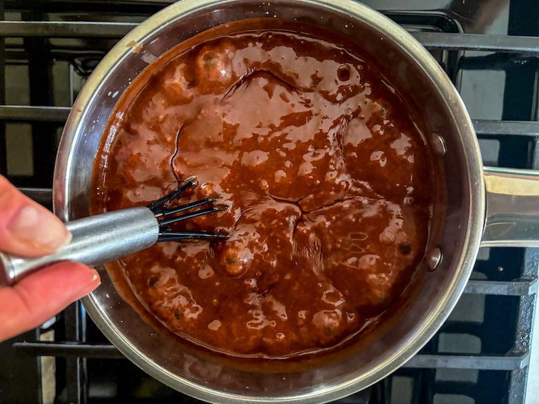 Hand whisking hot fudge sauce in a pan on the stovetop