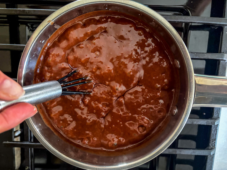 Hand whisking a pan of homemade hot fudge sauce on the stovetop
