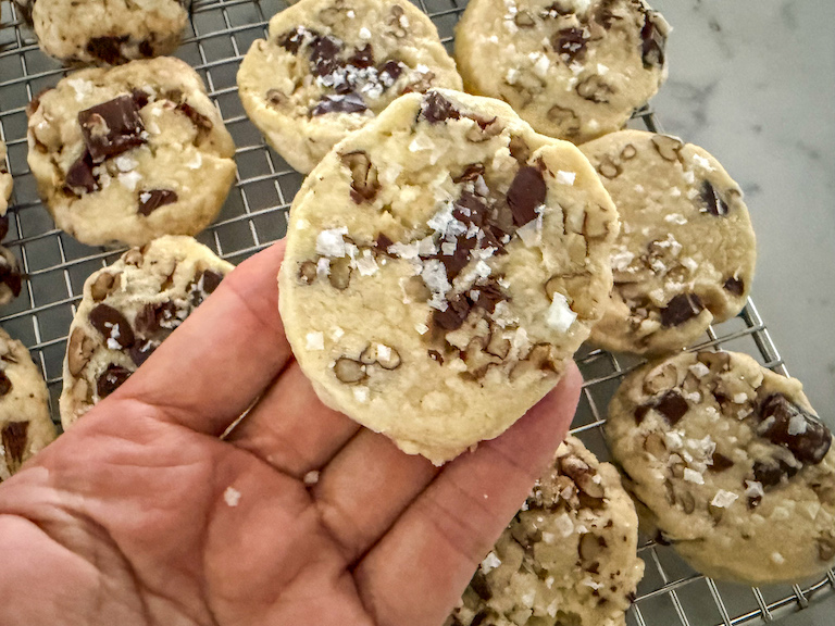 Hand holding a chocolate pecan shortbread cookie with sea salt