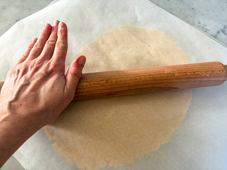 rolling pastry between sheets of parchment with a wooden rolling pin
