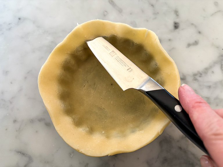 knife trimming excess pastry from a mini tart shell