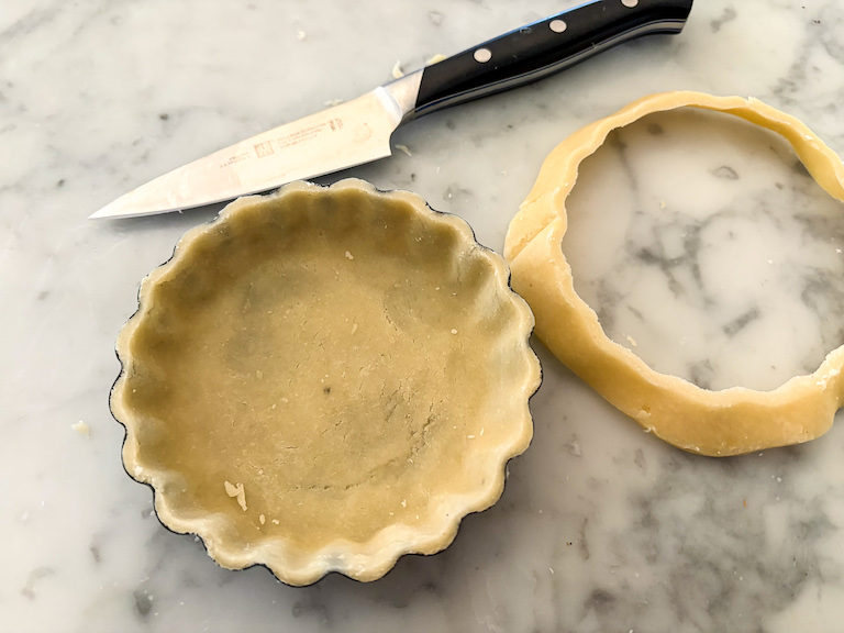 knife trimming excess pastry from a tartlet shell