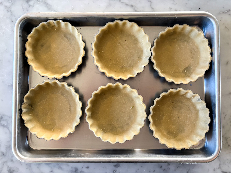 six miniature tart shells arranged on a small tray, before baking