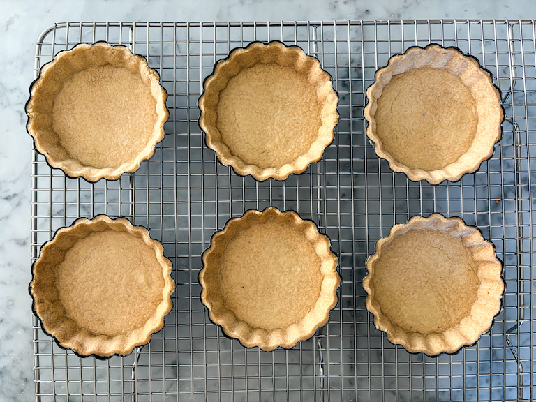 six mini tart shells cooling on a wire rack