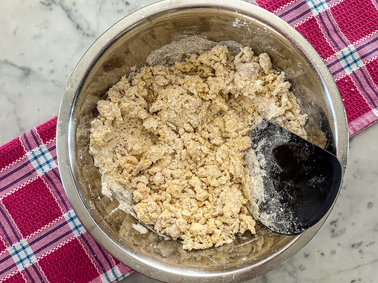 Bench scraper blending dough in a metal bowl