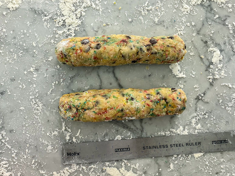 Ruler measuring logs of biscotti on a floured countertop