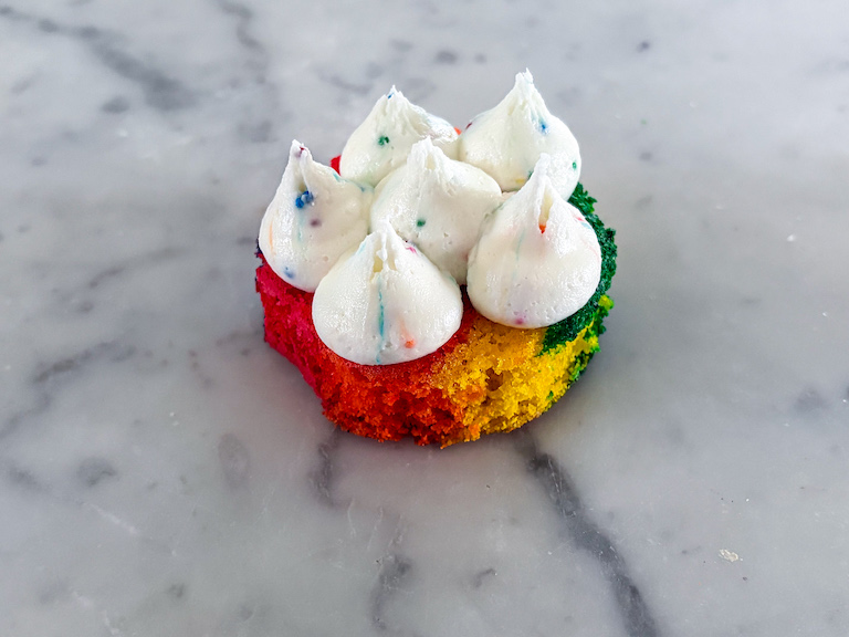 A small rainbow cake with dollops of buttercream piped on top