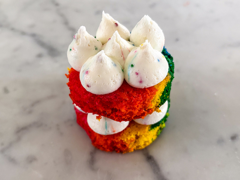 Piping buttercream on small discs of rainbow cake