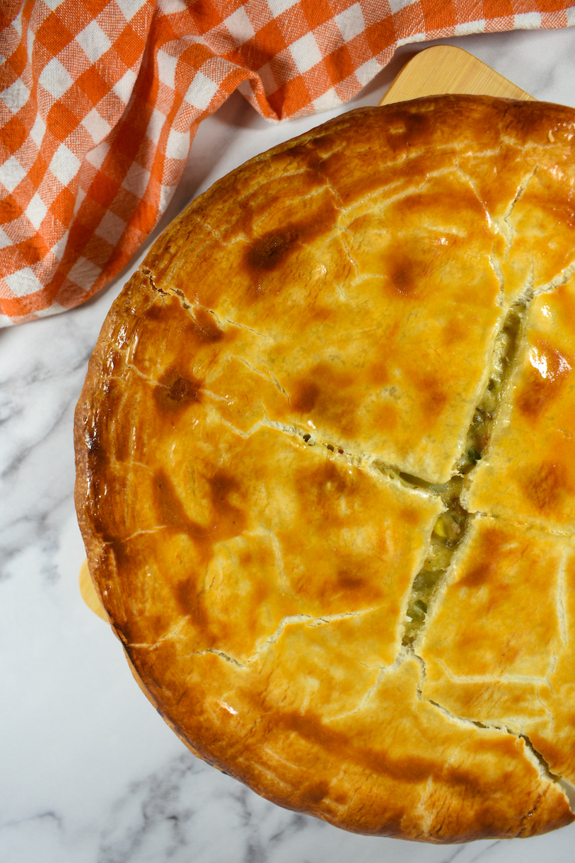 a pot pie with a golden brown crust, on a marble surface with an orange checkered towel