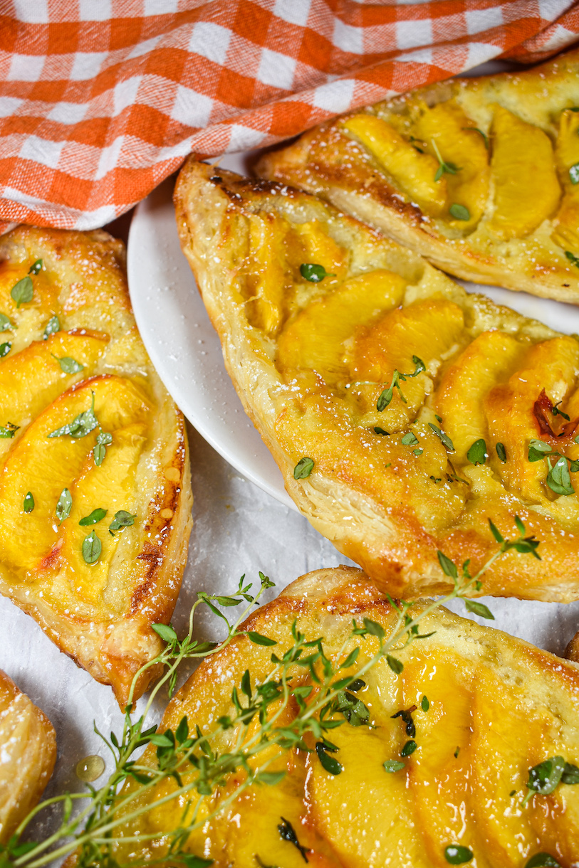 peach and mascarpone puff pastries on a white plate with orange checkered tea towel