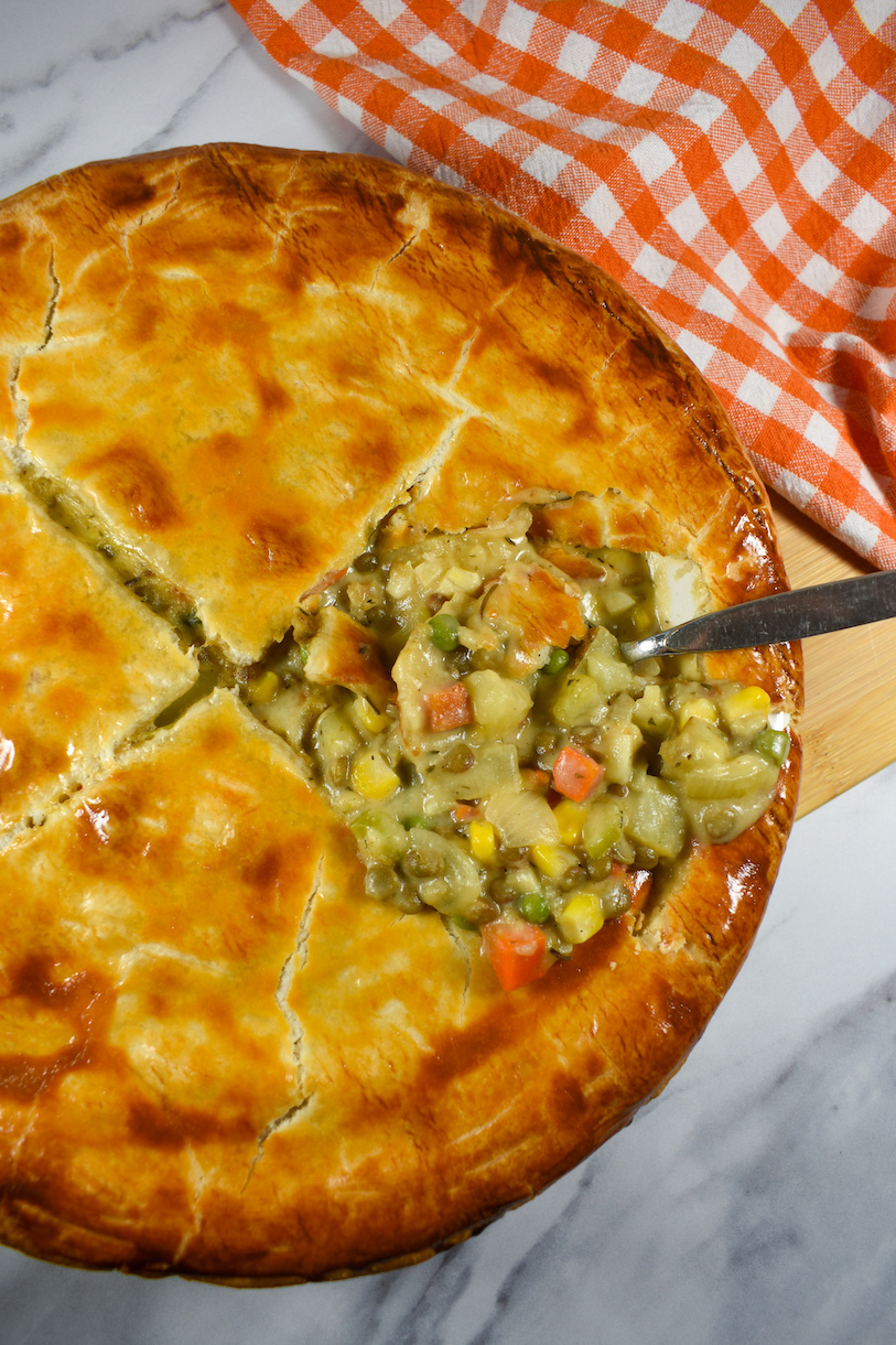 a meatless pot pie with a golden brown crust, on a marble surface next to an orange checkered tea towel
