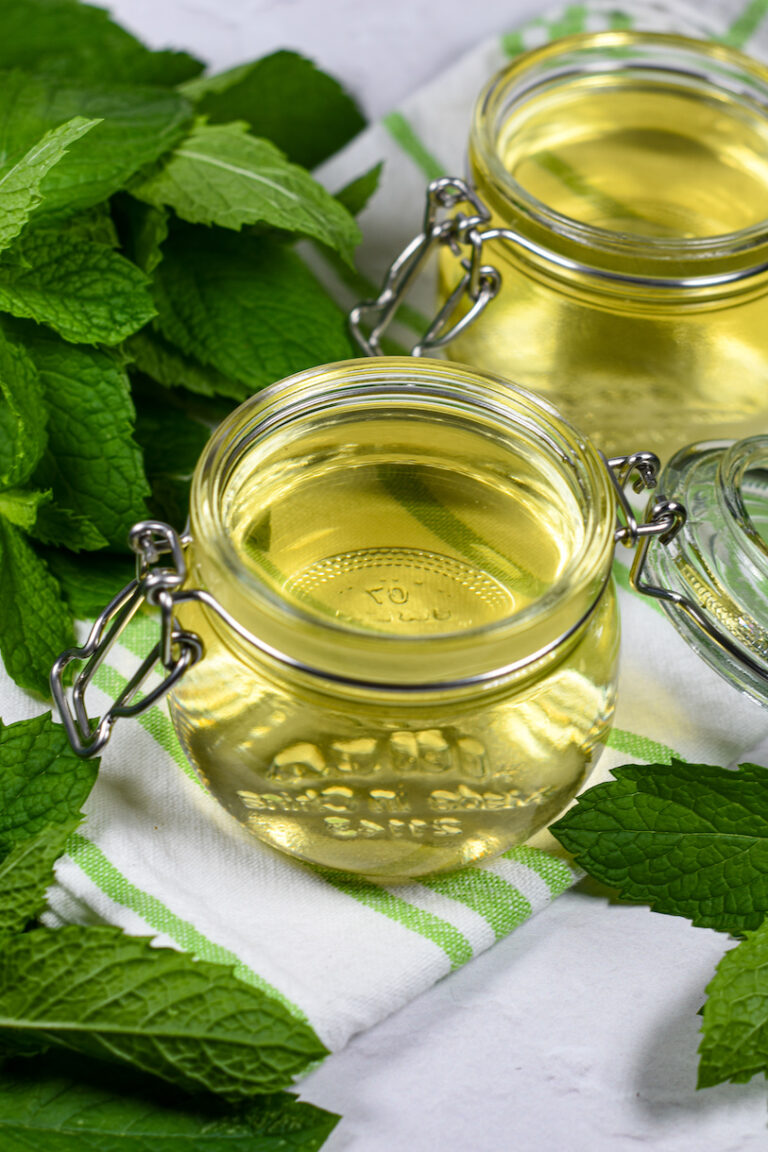 Jars of mint syrup surrounded by leaves of fresh mint
