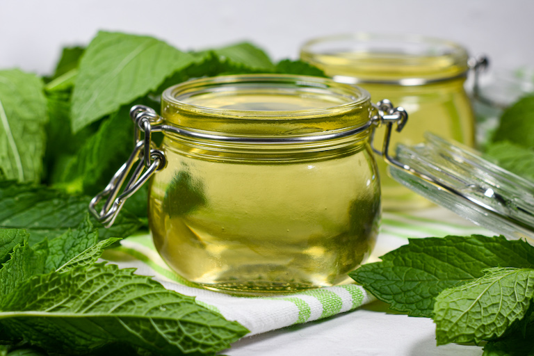 A glass jar of mint simple syrup surrounded by mint leaves