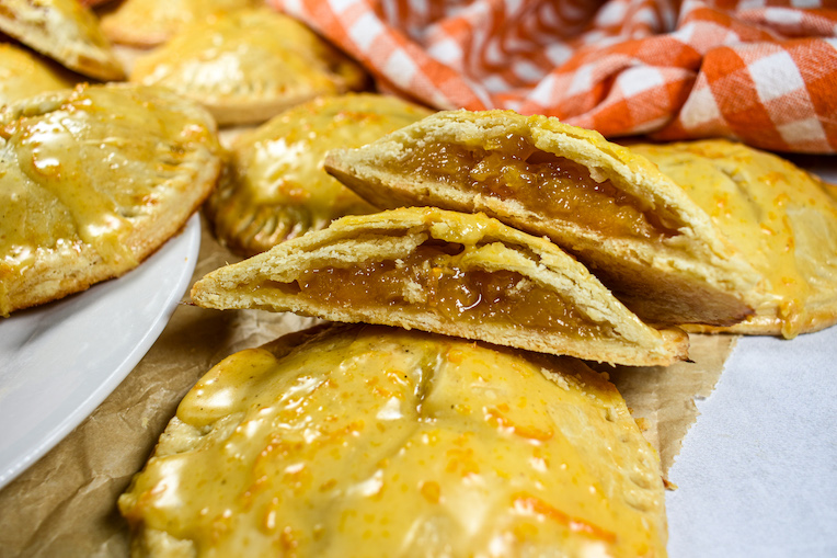 A sliced peach hand pie on a white surface with a checkered tea towel and sheet of parchment