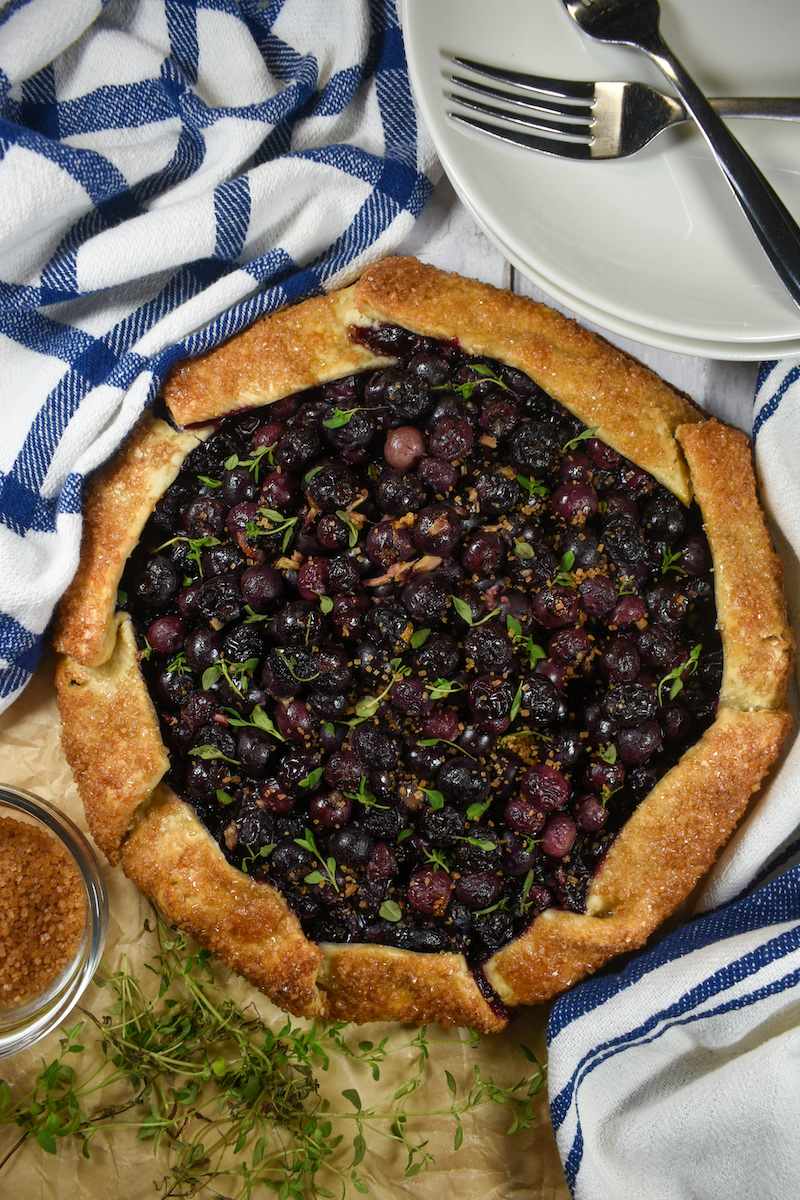 blueberry galette, plates, tea towels, and sprigs of fresh thyme