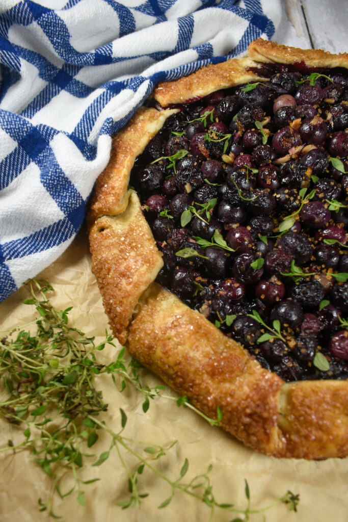 blueberry galette on a sheet of parchment with fresh thyme leaves