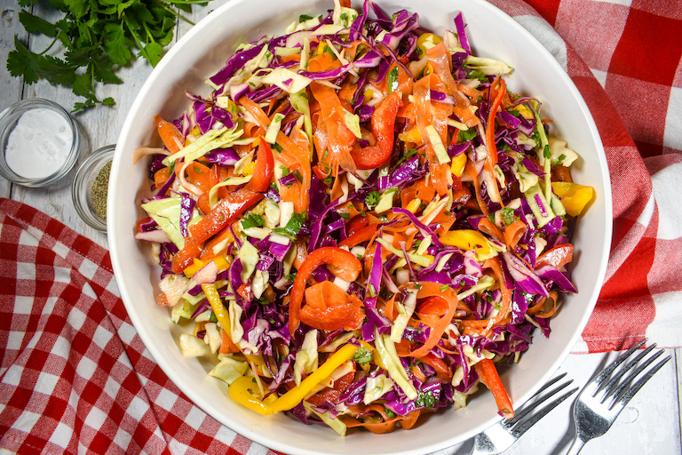 a bowl of rainbow coleslaw with red checkered tea towels