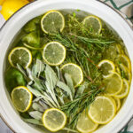 Herb and citrus simmer pot on a white surface with a plaid towel and yellow lemons